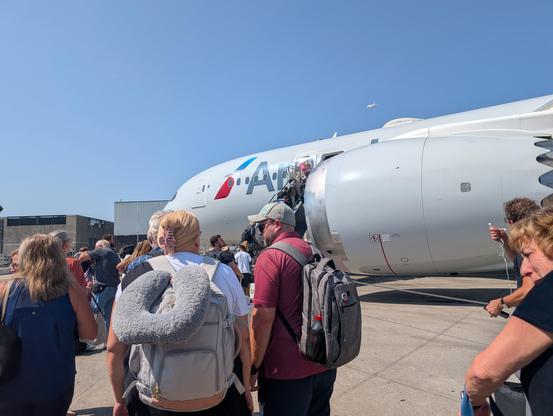 People boarding an American Airlines plane directly from the tarmac via stairs.