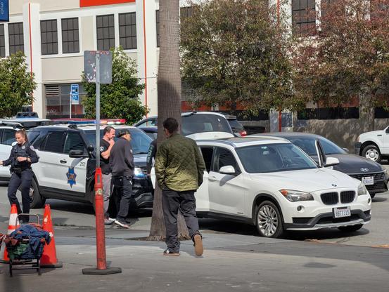 SFPD officer in green jacket looks at empty BMW.